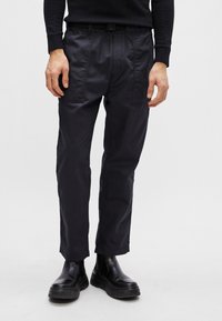 Calças pretas, ajustadas, com uma textura suave, apresentando costuras visíveis e bolsos, combinadas com botas pretas de plataforma robustas.