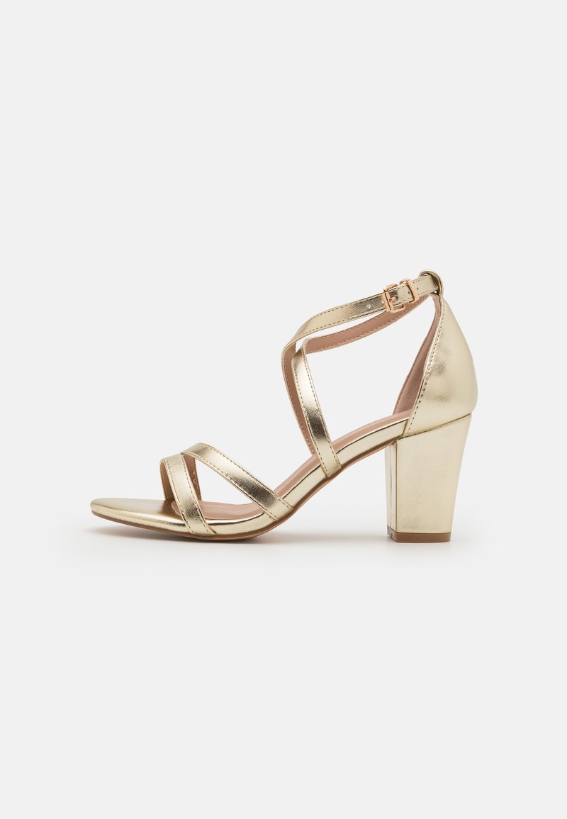 Gold heeled sandals with a block heel, featuring multiple metallic, crisscross straps and an ankle strap with a buckle.