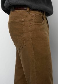 Pantalons en velours côtelé marron avec une coupe droite, dotés de poches arrière, d'une texture côtelée subtile et d'accents en métal contrastants.