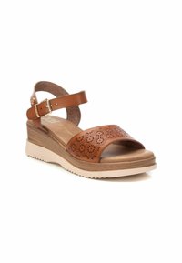Sandalia de cuña de cuero marrón con diseño floral perforado, plantilla acolchada y correa ajustable en el tobillo. Presenta una suela de goma beige.