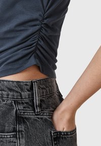 Navy blue fitted top with gathered detailing at the side, paired with high-waisted black and white striped denim jeans featuring front pockets.