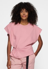 Lyserød T-shirt med korte ærmer, rund halsudskæring og samling ved taljen, lavet af blødt og let stof.