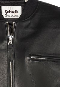 Giacca di pelle nera con zip frontale argentata e tasca con zip, caratterizzata da un'etichetta bianca Schott N.Y.C. all'interno del colletto.