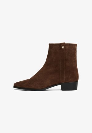Stivale alla caviglia in suede marrone con tacco nero basso e un piccolo logo metallico vicino alla parte superiore sul lato esterno.