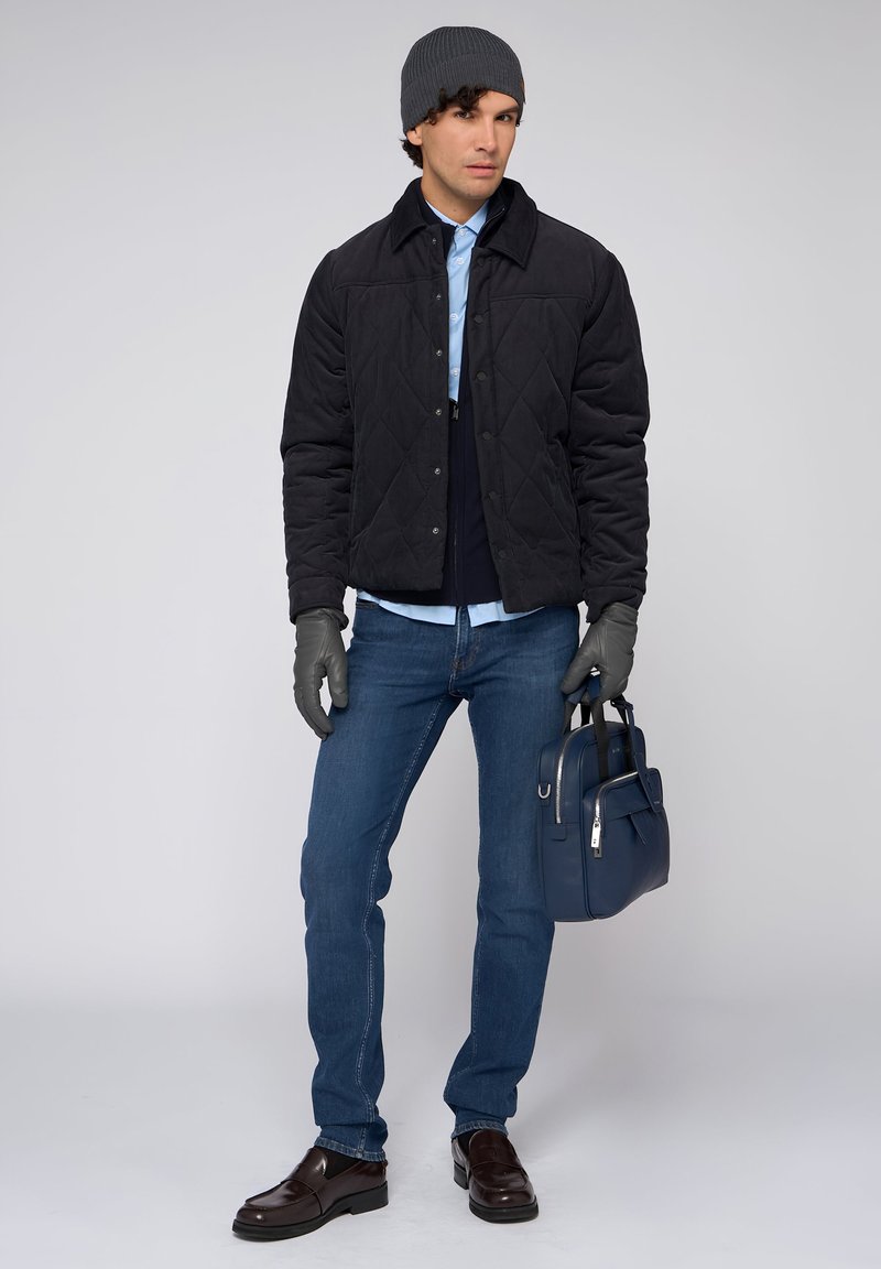 Czarna pikowana kurtka, niebieska koszula, granatowe dżinsy, szare rękawiczki i dopasowana czapka. Brązowe mokasyny i niebieska torba dopełniają strój.