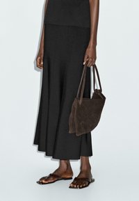Gonna nera alla caviglia in tessuto morbido, abbinata a una borsa tote in suede marrone scuro e sandali marroni piatti con cinturini sottili.