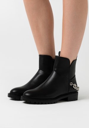 Botines negros de cuero liso con un panel lateral texturizado y un acento de cadena plateada. Presentan una punta redondeada y una suela resistente.