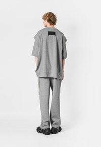 Camiseta gris oversized de manga corta, con un acento rectangular negro en la espalda. Combinada con pantalones grises a juego y zapatos negros texturizados.