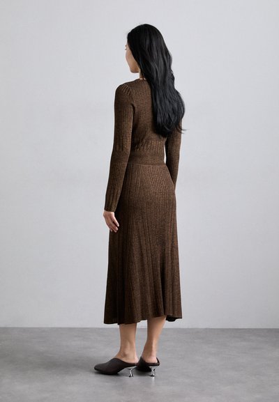 Brown ribbed knit dress with long sleeves, fitted bodice, and flared skirt. Worn with dark brown mules featuring silver heel accents.