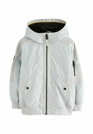 Hellgraue Jacke mit Kapuze, Reißverschluss vorne, zwei Seitentaschen, strukturierter Stoff und schwarzen Akzenten an den Ärmeln. Gelb gefüttertes Innere.