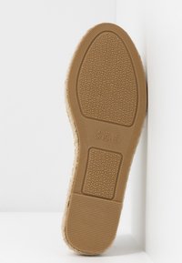 Brun gummisula med texturerat grepp, med ihåliga mönster och en kant av naturliga fibrer längs ovansidan. Storlekmarkeringar synliga.