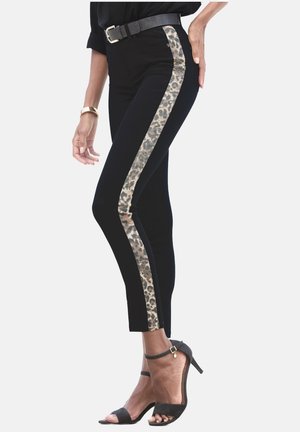 Schwarze Hose mit Leopardenmuster an den Seitenstreifen, schlanker Schnitt, ergänzt durch einen schwarzen Gürtel und Absatzsandalen.