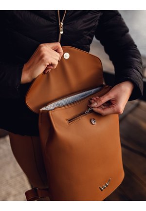 Brown leather backpack with a magnetic snap and a zippered interior pocket featuring a zigzag-patterned lining. Adjustable strap visible.