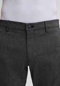 Pantaloni grigi dal tessuto strutturato con una vestibilità classica, dotati di chiusura con bottone e tessuto a motivo sottile. Nessun ulteriore dettaglio visibile.