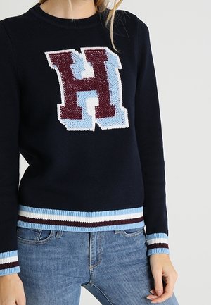 Pull en tricot marine avec un grand logo "H" multicolore. Manches et ourlet côtelés avec des rayures bleu et bourgogne. Coupe décontractée.