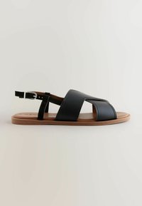 Sandales en cuir noir avec une semelle plate, dotées de brides croisées et d'une boucle à l'arrière. Dessus lisse et brides de soutien texturées.