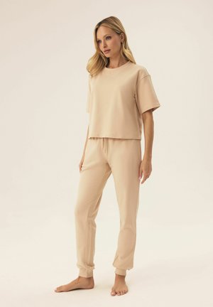 Beige Loungewear-Set mit locker sitzendem Kurzarmoberteil und tapered Hosen mit elastischen Bündchen. Weiche Textur mit entspanntem Design.