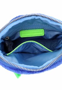 Borsa in tessuto blu con un esterno morbido; l'interno presenta una fodera azzurro chiaro liscia, dettagli verdi e un compartimento con zip.
