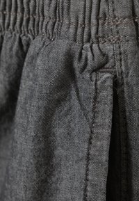 Tissu gris avec une taille froncée élastique, texture lisse et couture contrastante le long des coutures. Design global décontracté.