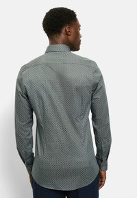 Herren-Langarmhemd aus dunkelgrünem Stoff mit geometrischem Muster. Verfügt über einen klassischen Kragen und geknöpfte Manschetten. Taillierte Passform.