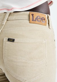 Beige kordjeans med en läderpatch från Lee på midjan, med subtil ribbkänsla och en liten logotyp på bakfickan.