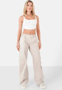 Witte geribbelde crop top met vierkante halslijn, gecombineerd met beige cargobroek met zijzakken en een ontspannen pasvorm, afgemaakt met witte sneakers.
