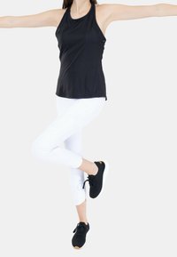 Zwarte sportieve tanktop, witte leggings en zwarte sneakers. De tanktop heeft een halternekontwerp, gladde stof en een aansluitende snit.