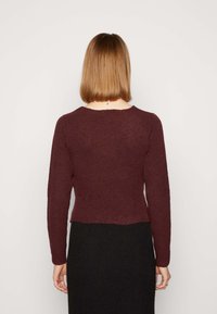 Bordeaux ribbel gebreid sweater met lange mouwen en een ronde halslijn, gedragen met een zwarte structuur rok. De achterkant toont de details van de stof.