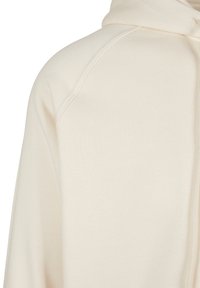 Sudadera con cremallera en tela color crema claro. Presenta un acabado texturizado, mangas raglán y capucha con cordón. Sin patrones ni herrajes visibles.