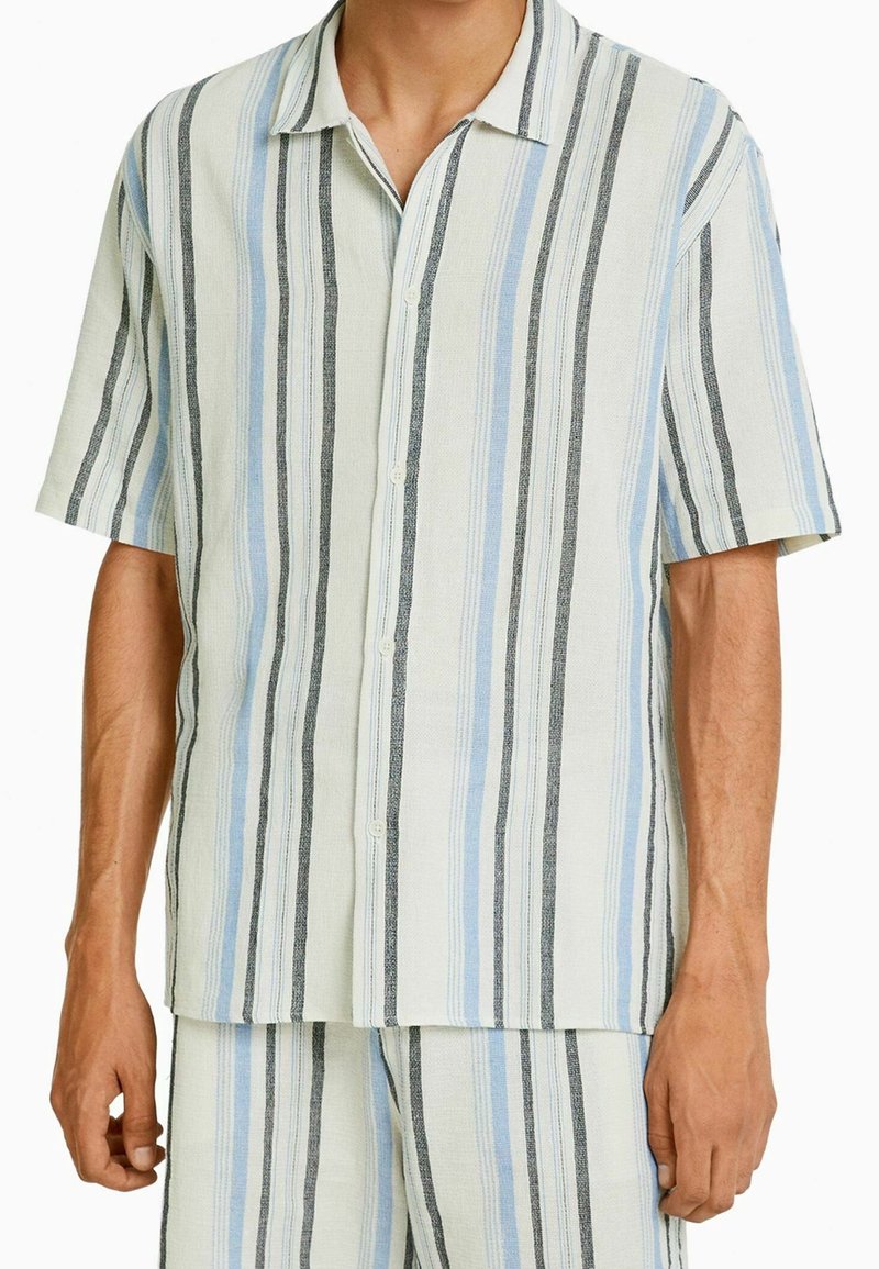 Camisa de botones de manga corta hecha de una tela ligera con rayas verticales en azul claro, negro y crema. Textura suave, corte relajado.