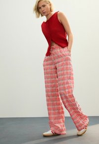 Röd texturerad ärmlös topp som matchas med lösa rosa rutiga byxor med dragsko i midjan. Modellen bär ljusa sneakers.