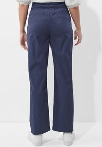 Marineblaue, weite Hosen mit elastischem Bund, aus glattem Material, geradem Schnitt und minimalen Nähten. Weiße Sneaker.