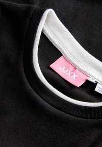 Black cotton T-shirt with a white collar, featuring a pink label with "JUXX." Texture is smooth and fabric appears soft.