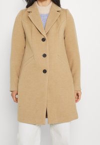 Abrigo de lana de camello con un diseño ajustado, solapas de muesca, tres botones oscuros y bolsillos laterales. Textura suave y corte a la altura de la rodilla.