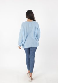 Pullover oversized di colore azzurro chiaro in maglia, con una finitura testurizzata, abbinato a jeans slim e sandali con tacco trasparente, visto da dietro.