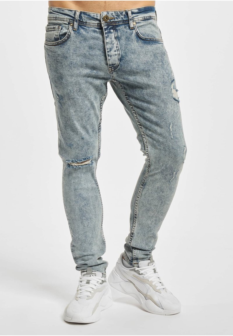 Lyseblå denimjeans med smal passform, med slitte detaljer og revne knær. Kombinert med hvite joggesko.