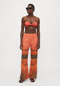 Top corto naranja con estampado de palmeras negras y detalle anudado, combinado con pantalones de pierna ancha a juego que presentan un diseño de atardecer degradado.