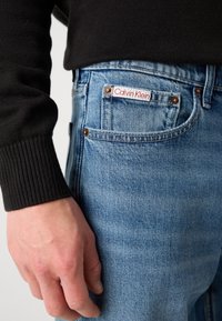 Lys blå denimjeans med en rød og hvit Calvin Klein-merkelapp på baklommen, med kobberbeslag og en klassisk passform.