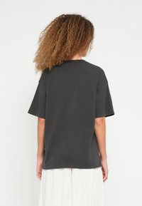 Tumehall, üle suurusega lühikeste varrukatega t-särk, valmistatud pehmest puuvillast, ümar kaelusega ja lõdva istuvusega, tagantpoolt vaadatuna.