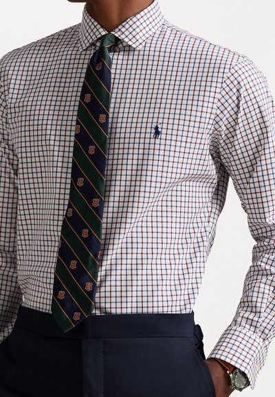Camisa de cuadro blanco con detalles en rojo y azul marino, acompañada de una corbata verde oscura con rayas diagonales y patrones de escudo.