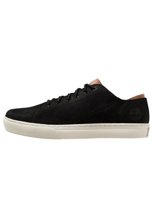 Baskets basses noires à lacets avec semelle blanche et détails en cuir marron clair au talon et à la languette, logo embossé visible sur le côté.