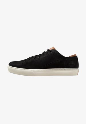 Baskets basses noires à lacets avec semelle blanche et détails en cuir marron clair au talon et à la languette, logo embossé visible sur le côté.