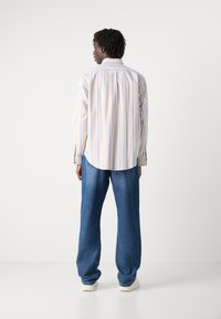 Lange mouwen shirt met lichtromige en blauwe verticale strepen, voorzien van een relaxte pasvorm en een afgeronde zoom, gecombineerd met loszittende blauwe jeans en witte schoenen.