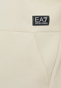 Bežinė džemperis su priekine kišene ir juodu EA7 Emporio Armani logotipo pleistru. Lygus, medvilnės mišinys su laisvu dizainu.