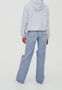 Ljusblå kort jacka med huva, kombinerad med ljusblå, sliten vida jeans. Detaljer inkluderar avslappnad passform och uppvikta ärmar.