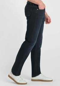 Jean en denim bleu foncé avec une coupe slim, présentant un design classique à cinq poches, des coutures discrètes et une texture lisse. Assorti avec des baskets blanches.