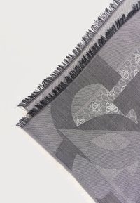 Γκρι ύφασμα με υφαντά αφηρημένα γεωμετρικά σχέδια και μαύρες κρόσσια στις άκρες, απεικονισμένο διαγώνια σε λευκό φόντο.