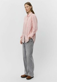 Ljusrosa skjorta med knappar och långa ärmar samt bröstficka, i kombination med grå vida jeans och bruna stövlar. Slät tygtextur.