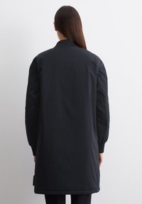 Długi czarny bomber made z lekkiego, teksturowanego materiału. Posiada prążkowany kołnierz i mankiety, gładkie wykończenie oraz wydłużoną długość.