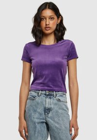 Paarse fluwelen t-shirt met korte mouwen, ronde hals, getailleerd ontwerp, gecombineerd met high-waisted lichte denim jeans. Zachte textuur.